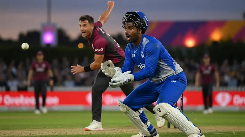 Close sideline frame of a batter in coloured kit driving through the off side under stadium lights with a blurred crowd behind